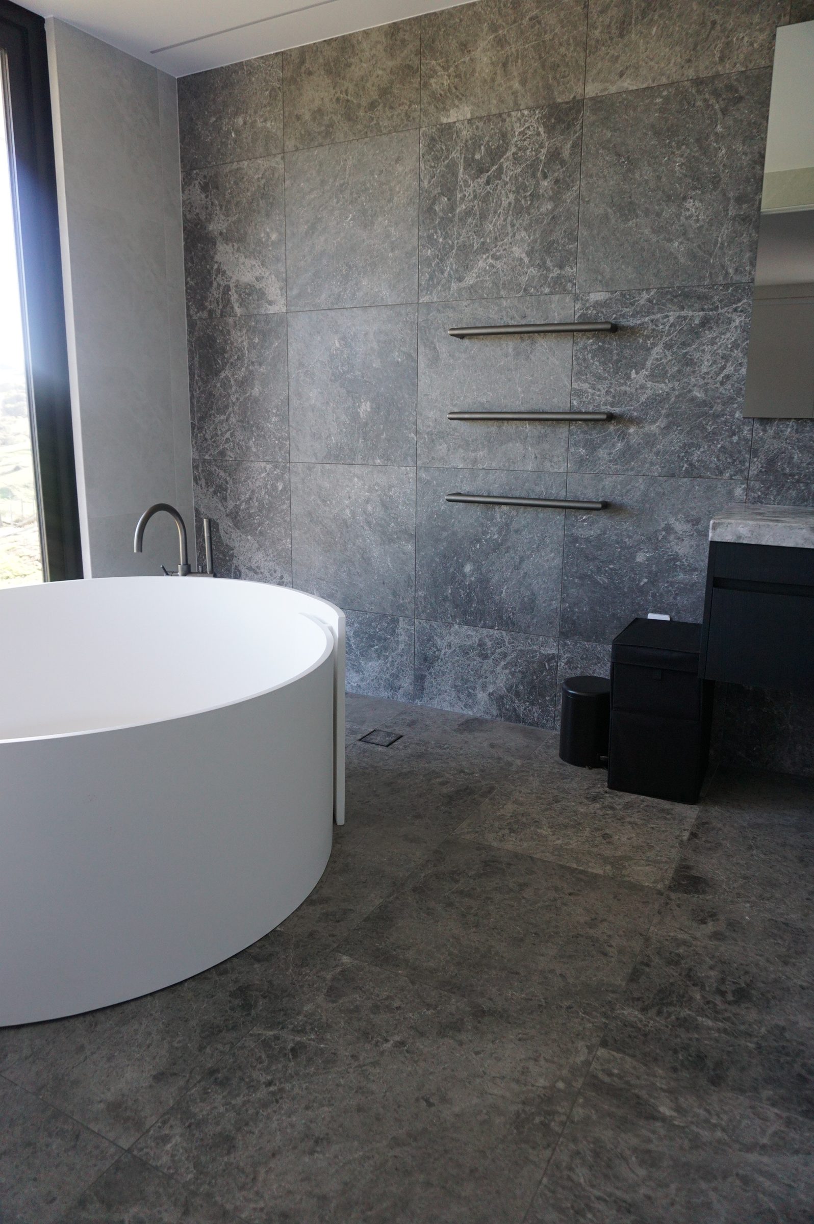 Blue limestone wall and floor tiles beside a round freestanding bath, Wainui, Gisborne