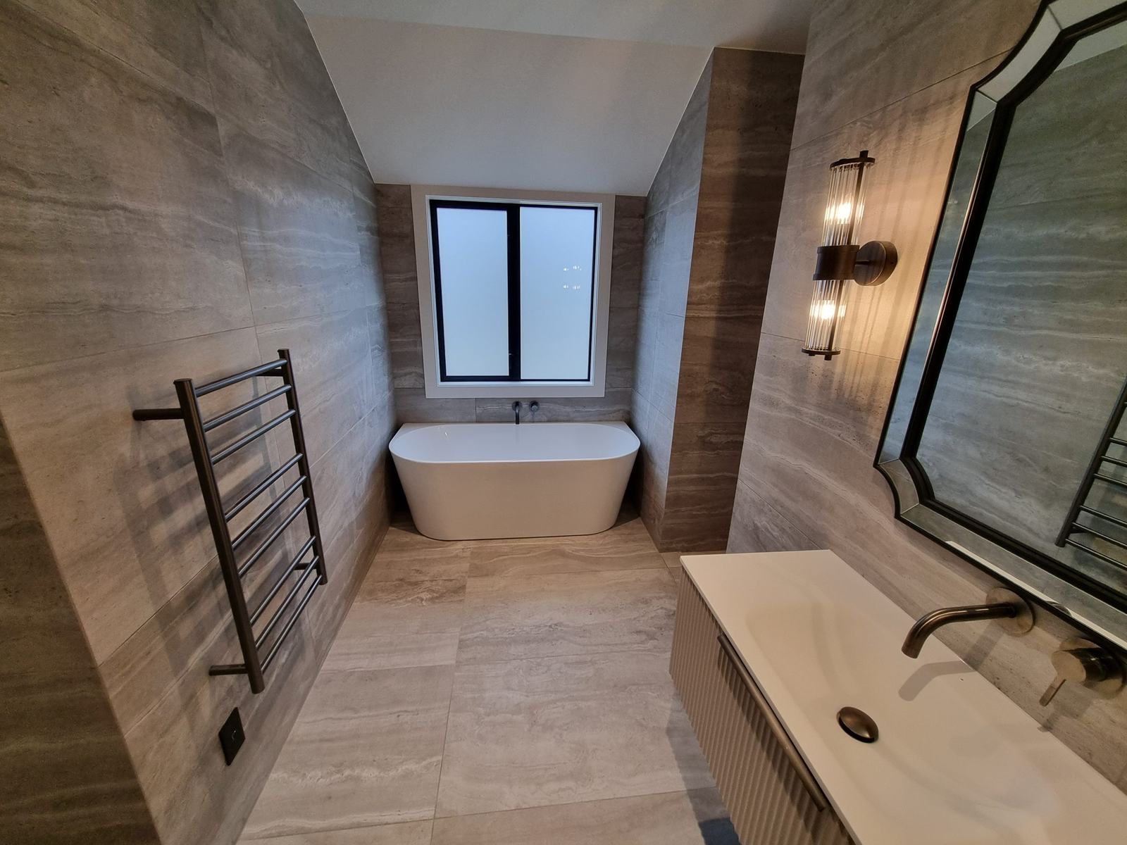 Large-format porcelain tiled bathroom with freestanding bath, heated towel rail and fluted vanity