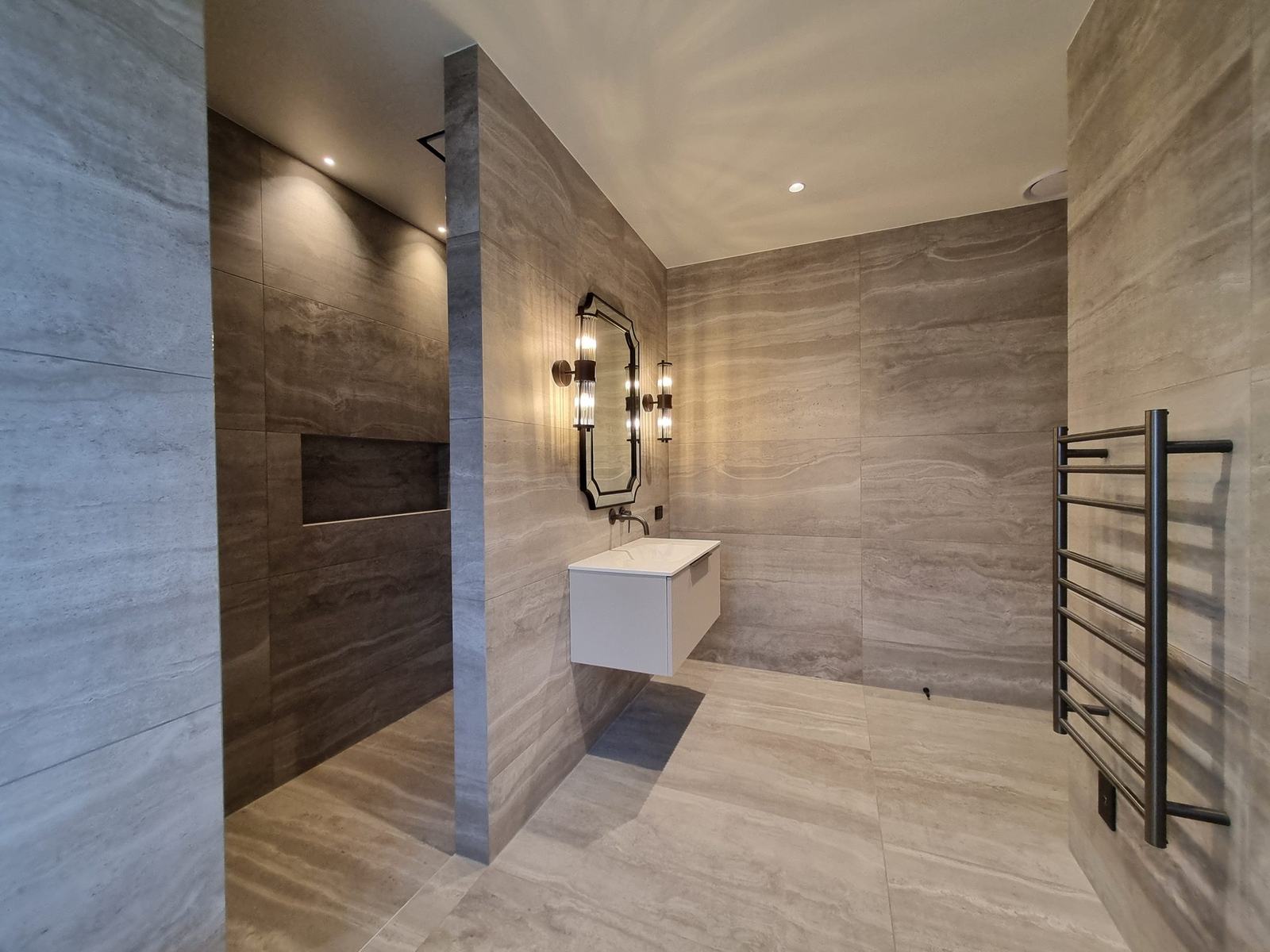 Large-format porcelain tiled walk-in shower with recessed niche beside a floating vanity and heated towel rail