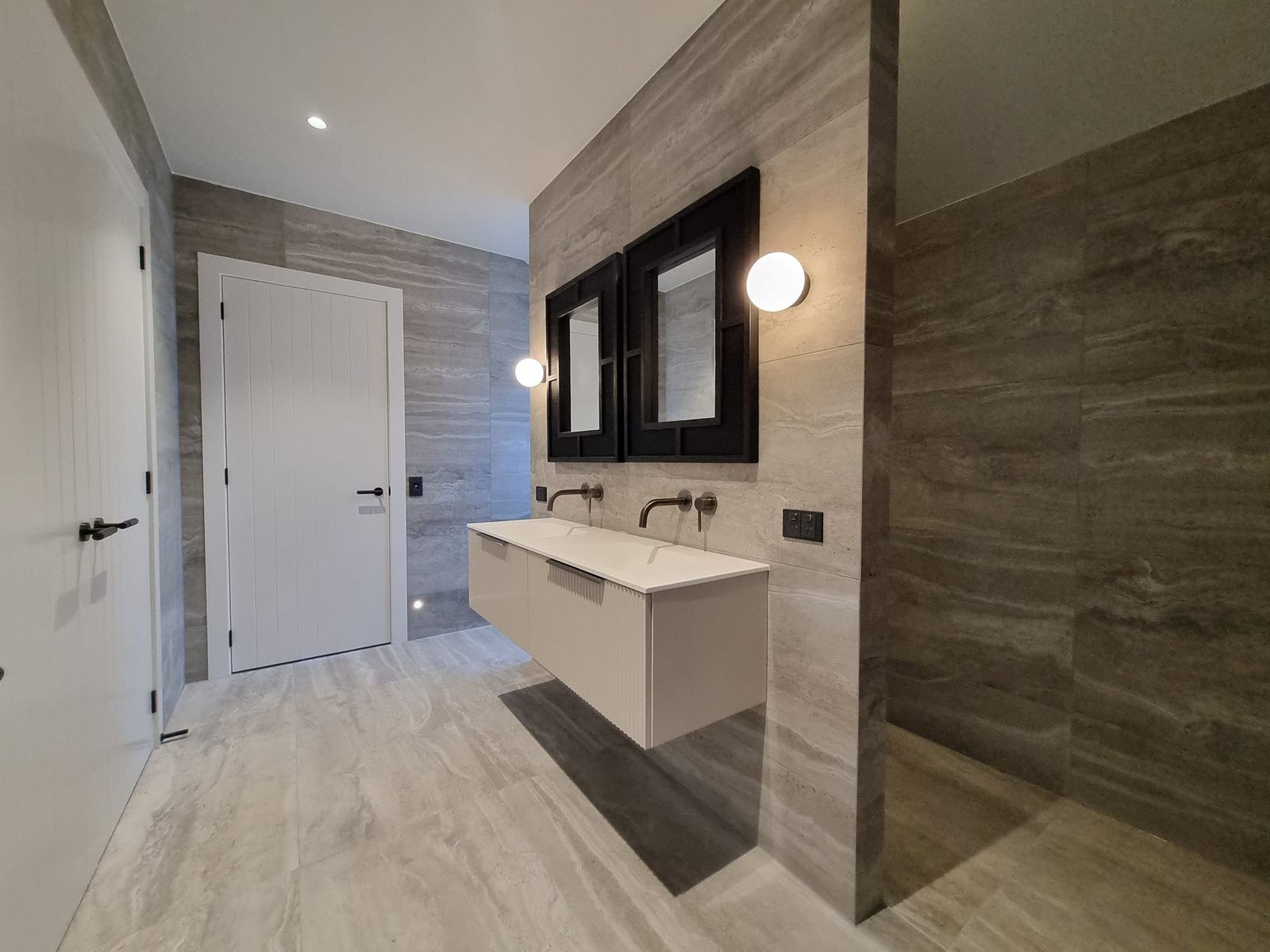 Large-format porcelain tiled bathroom with floating double vanity, black framed mirrors and walk-in shower