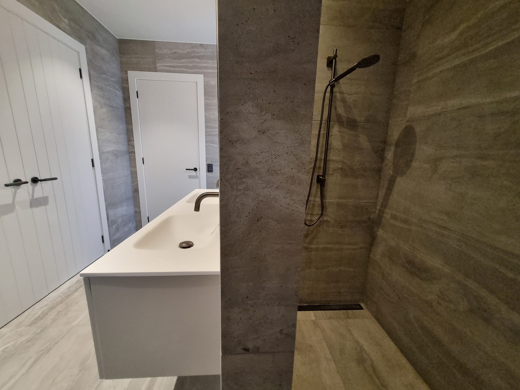 Palmer Mill bathroom with a floating vanity beside a walk-in shower with slide rail, linear drain and large-format travertine-look tile