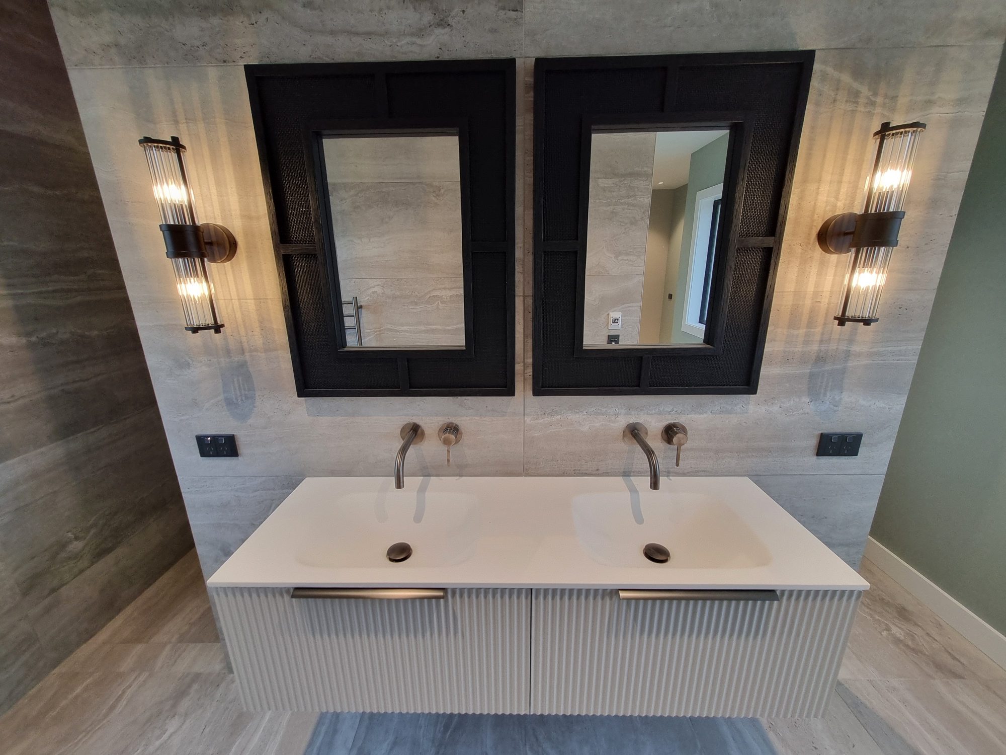 Floating fluted double vanity with two wall-mounted taps, black framed mirrors and glass wall lights against large-format tile