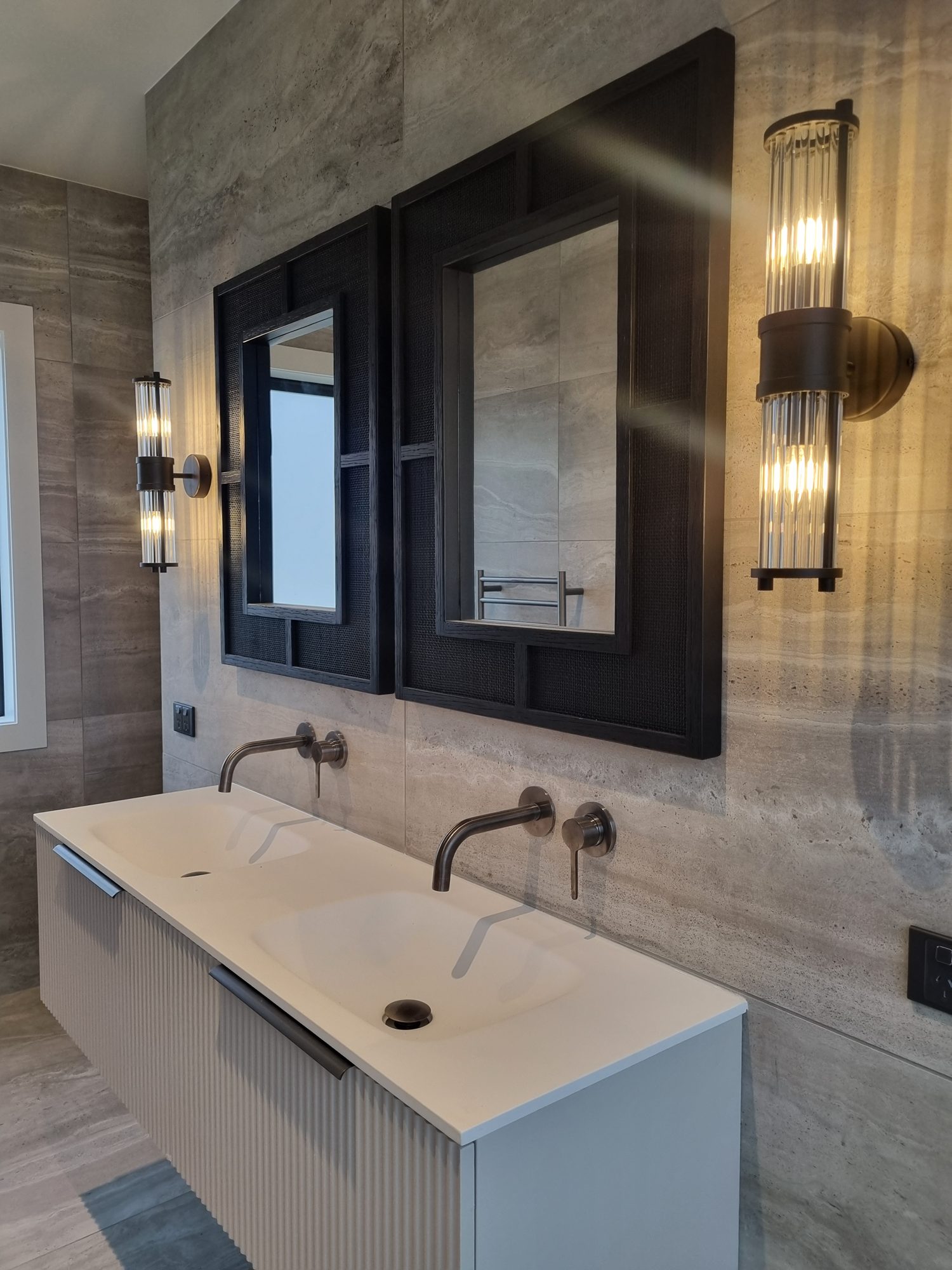Floating fluted double vanity with black framed mirrors and glass wall lights against large-format travertine-look tile, Palmer Mill master ensuite