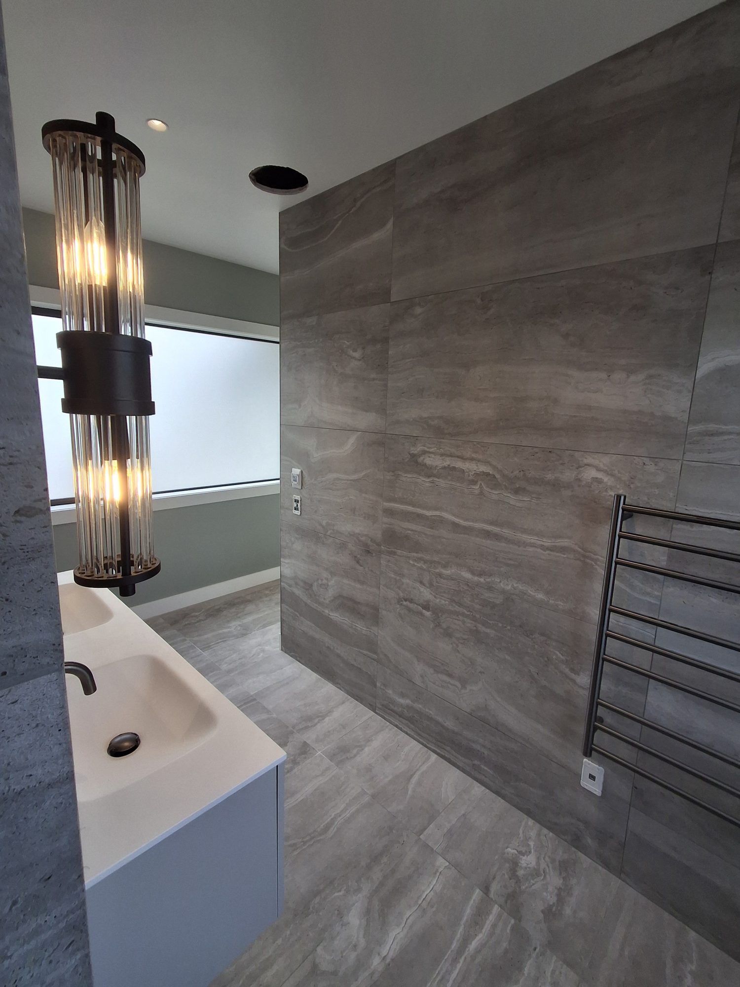 Large-format travertine-look tiled wall and floor with a heated towel rail and glass pendant light in the Palmer Mill master ensuite