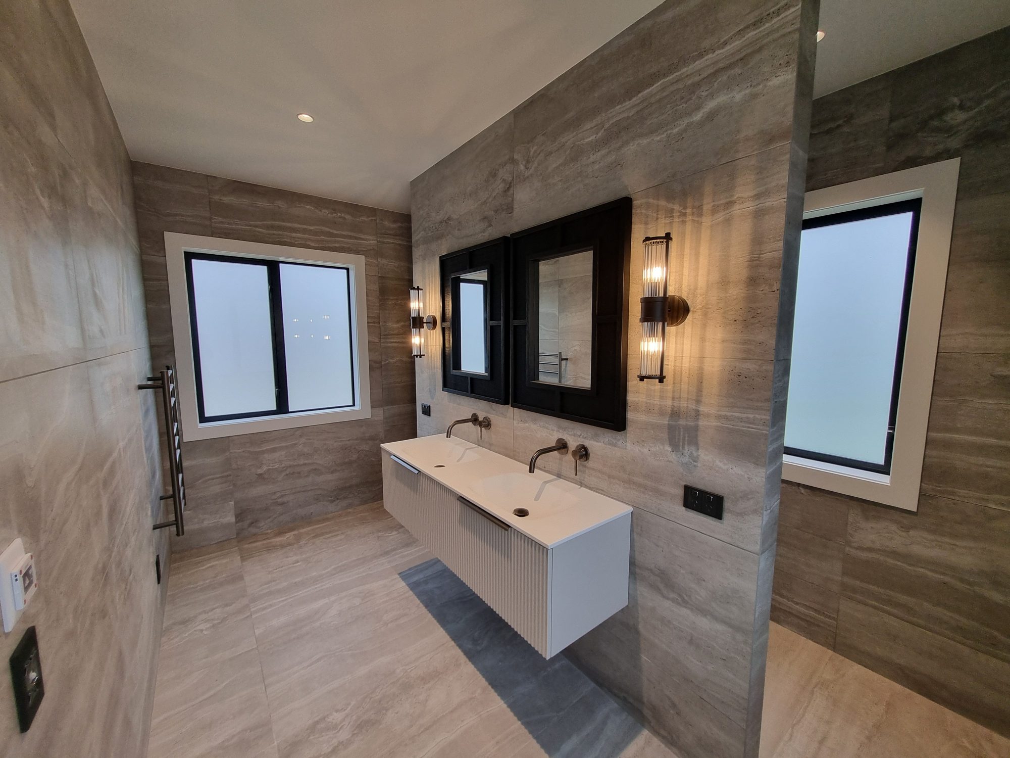 Wide view of the Palmer Mill master ensuite, with large-format tile on the floor and walls, a floating double vanity and heated towel rail