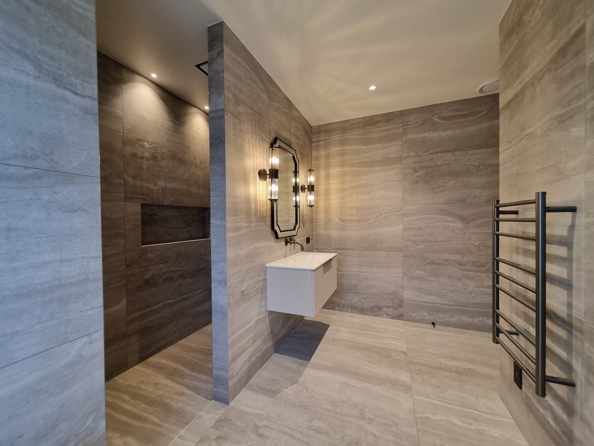 Palmer Mill guest ensuite with an open shower and recessed niche, floating vanity, shaped mirror and glass wall lights in large-format tile