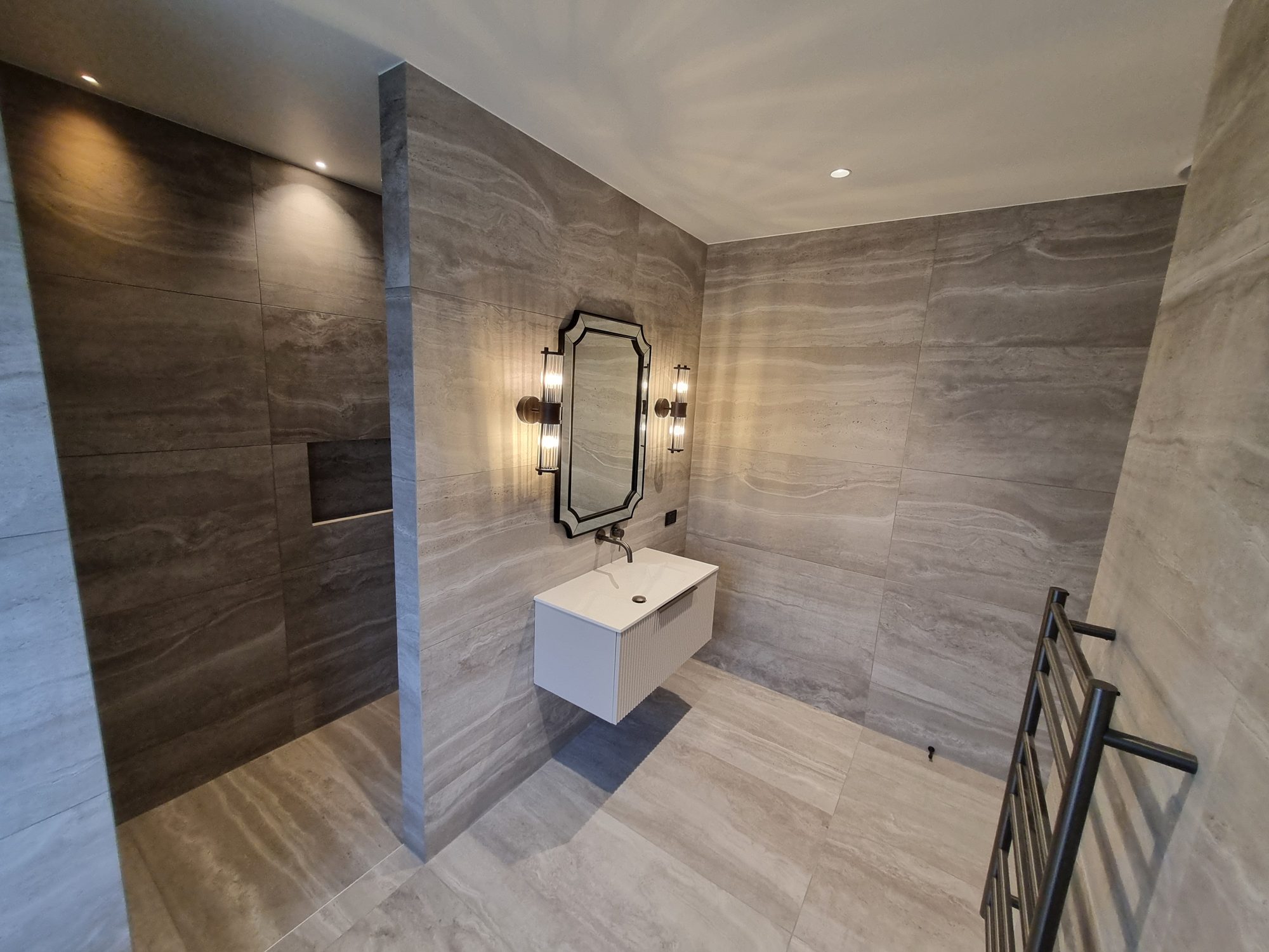 Palmer Mill guest ensuite with large-format travertine-look tile on the floor and walls, an open shower, floating fluted vanity, shaped mirror and heated towel rail