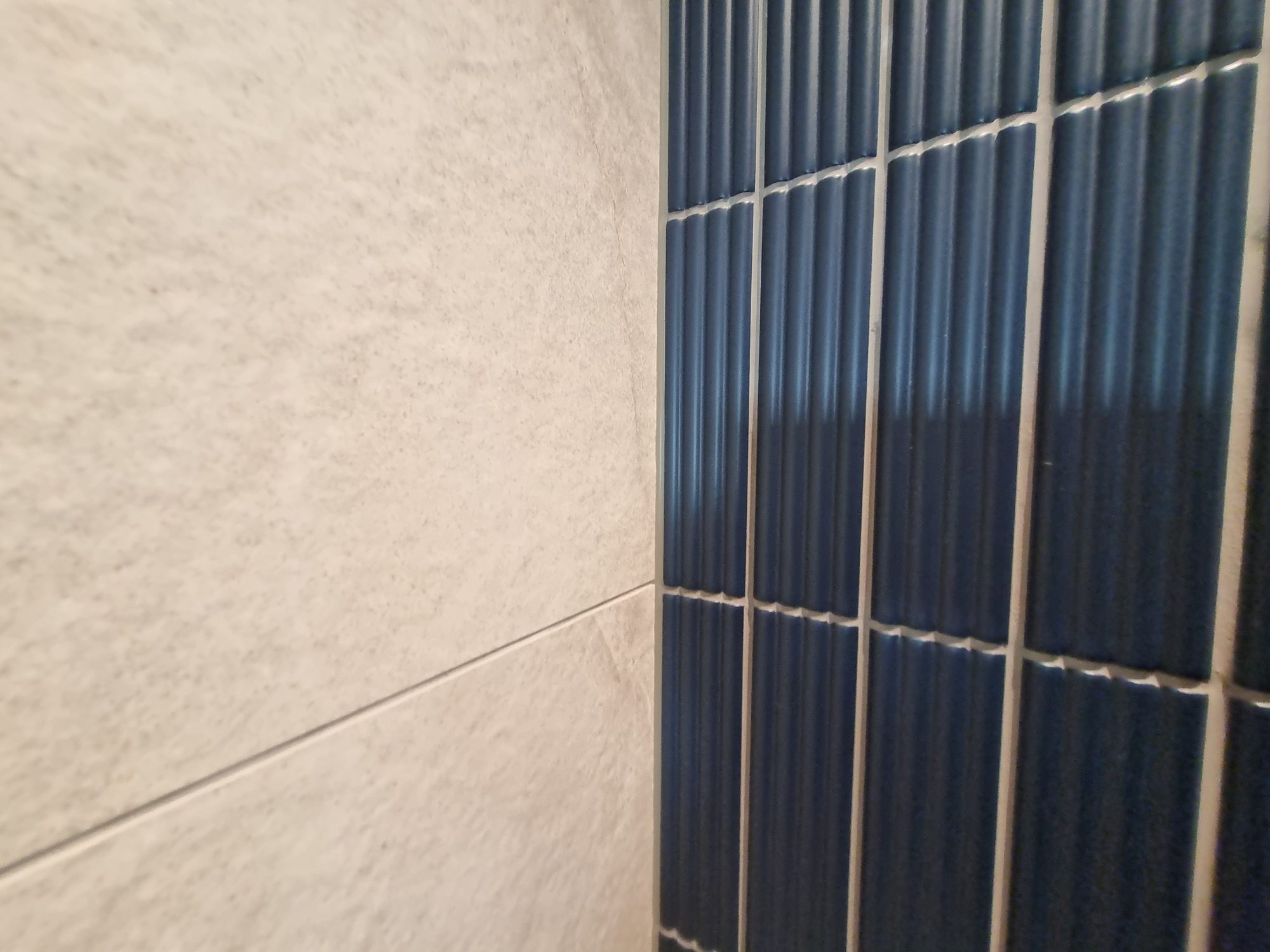 Close-up of the corner where large-format textured wall tile meets fluted blue tile with neat, even grout lines